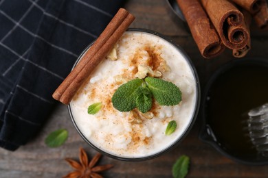 Photo of Tasty rice pudding with cinnamon, mint and nuts on wooden table, flat lay