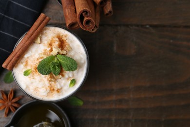 Photo of Tasty rice pudding with cinnamon, mint and nuts on wooden table, flat lay. Space for text