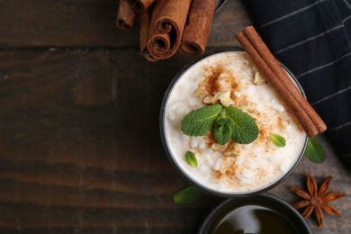 Photo of Tasty rice pudding with cinnamon, mint and nuts on wooden table, flat lay. Space for text