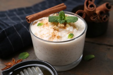 Photo of Tasty rice pudding with cinnamon, mint and nuts on wooden table, closeup