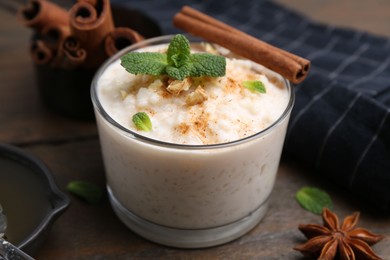 Photo of Tasty rice pudding with cinnamon, mint and nuts on wooden table, closeup