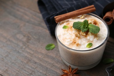 Photo of Tasty rice pudding with cinnamon, mint and nuts on wooden table, closeup. Space for text