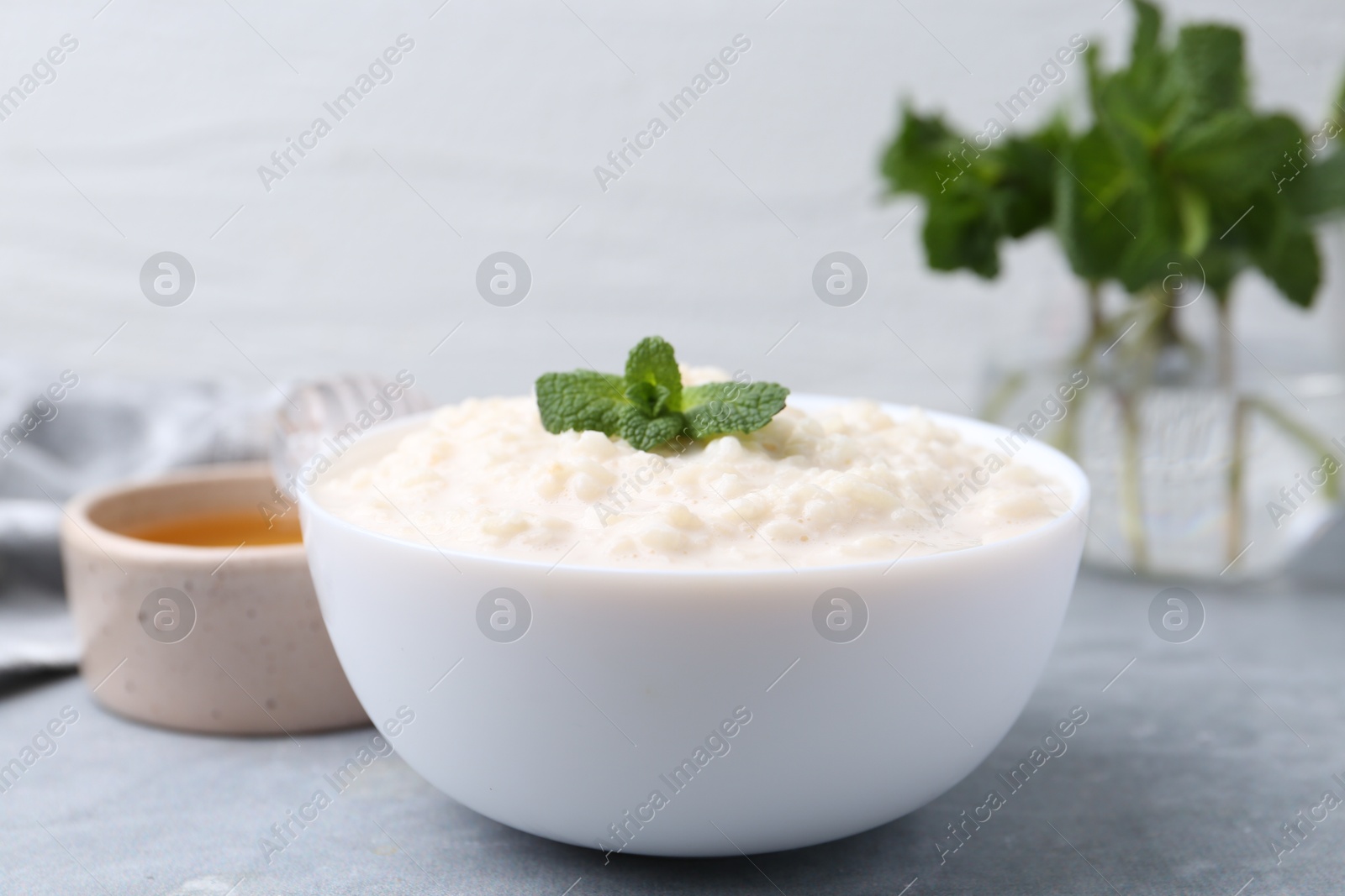 Photo of Tasty rice pudding with mint and honey on light grey table, closeup