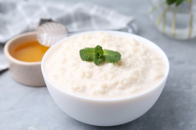 Photo of Tasty rice pudding with mint and honey on light grey table, closeup