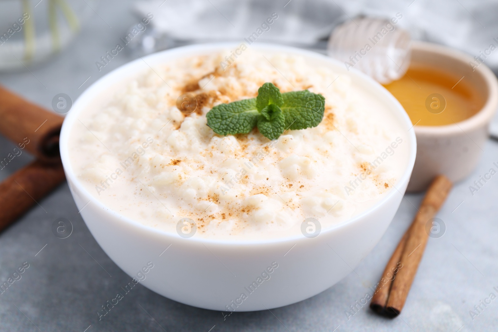 Photo of Tasty rice pudding with cinnamon, mint and honey on light grey table, closeup