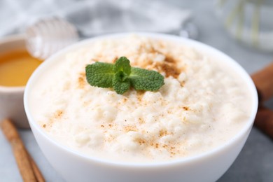 Photo of Tasty rice pudding with cinnamon, mint and honey on light grey table, closeup