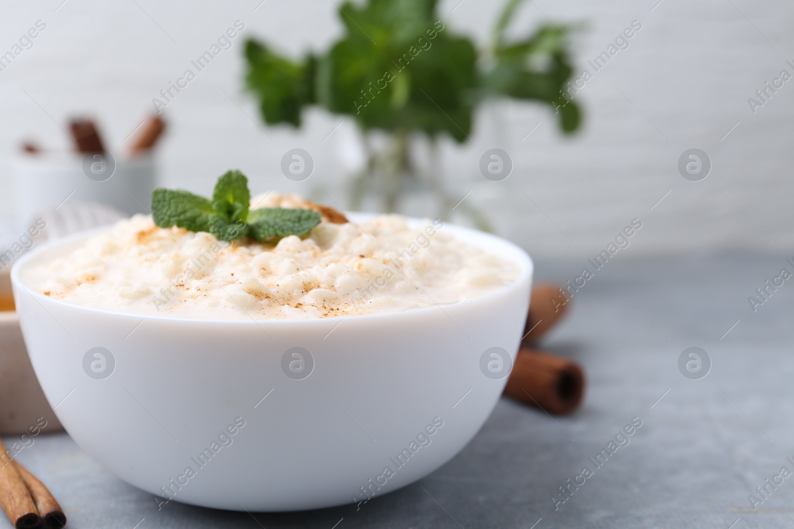 Photo of Tasty rice pudding with cinnamon and mint on light grey table, closeup. Space for text