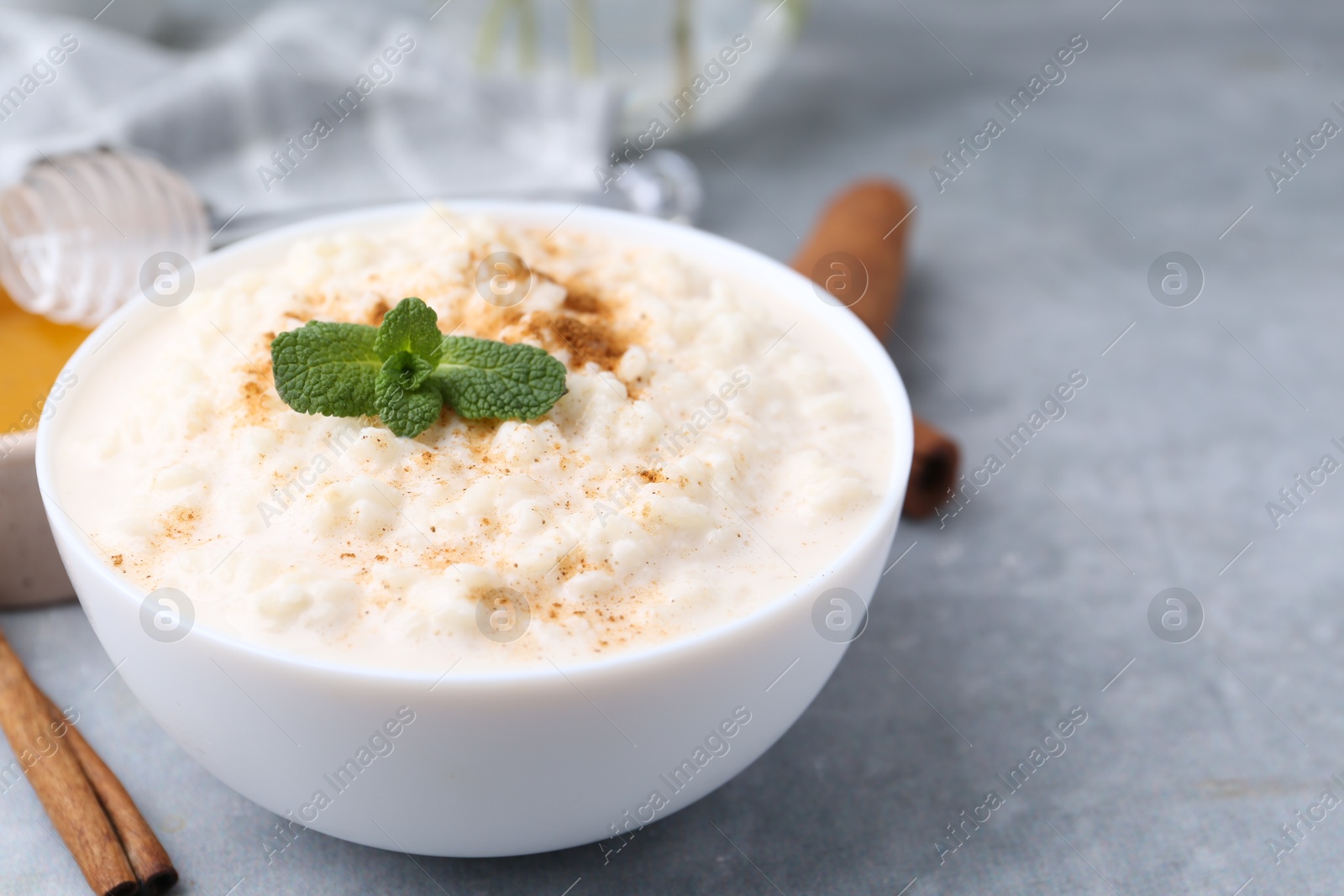 Photo of Tasty rice pudding with cinnamon and mint on light grey table, closeup. Space for text