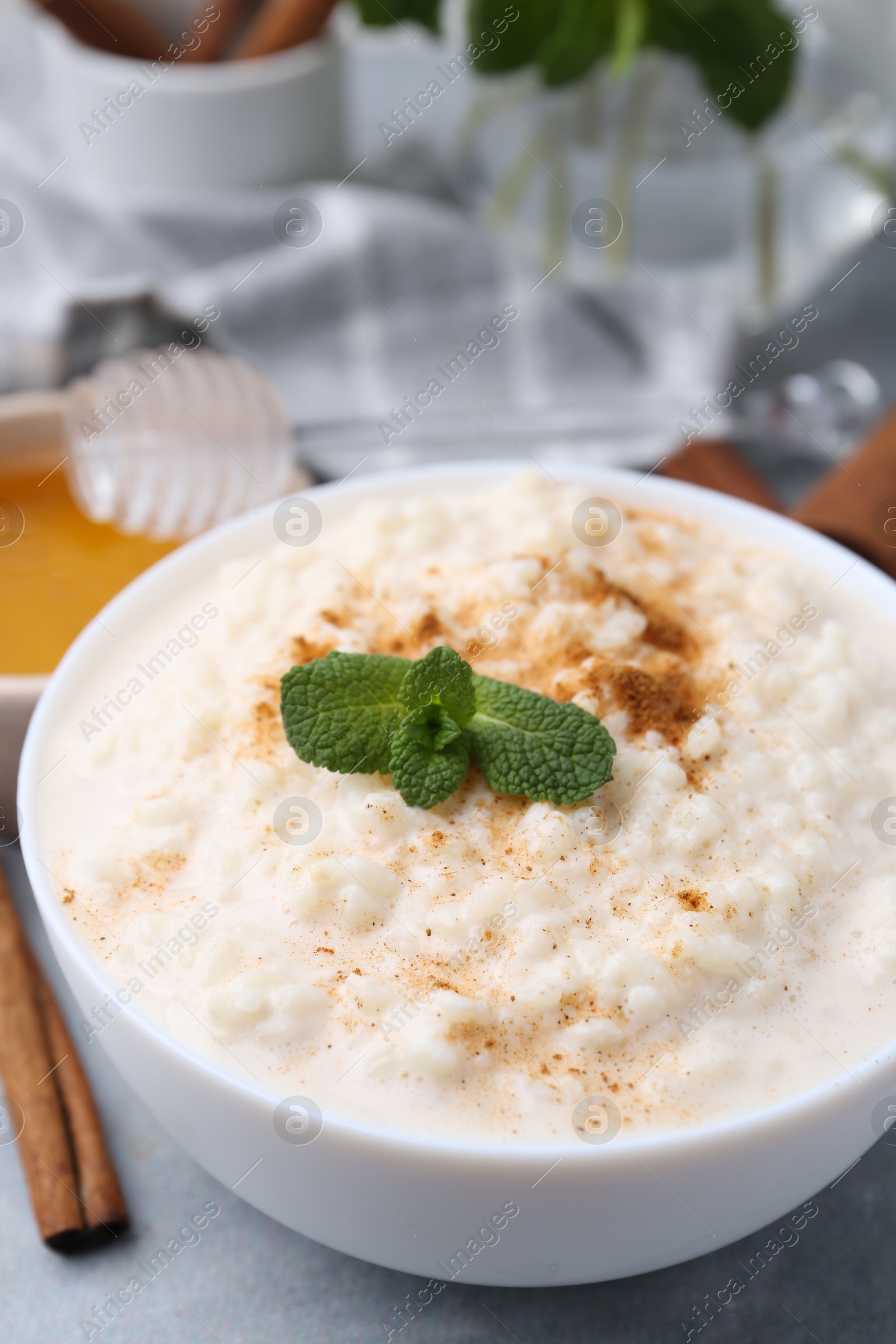 Photo of Tasty rice pudding with cinnamon, mint and honey on light grey table, closeup