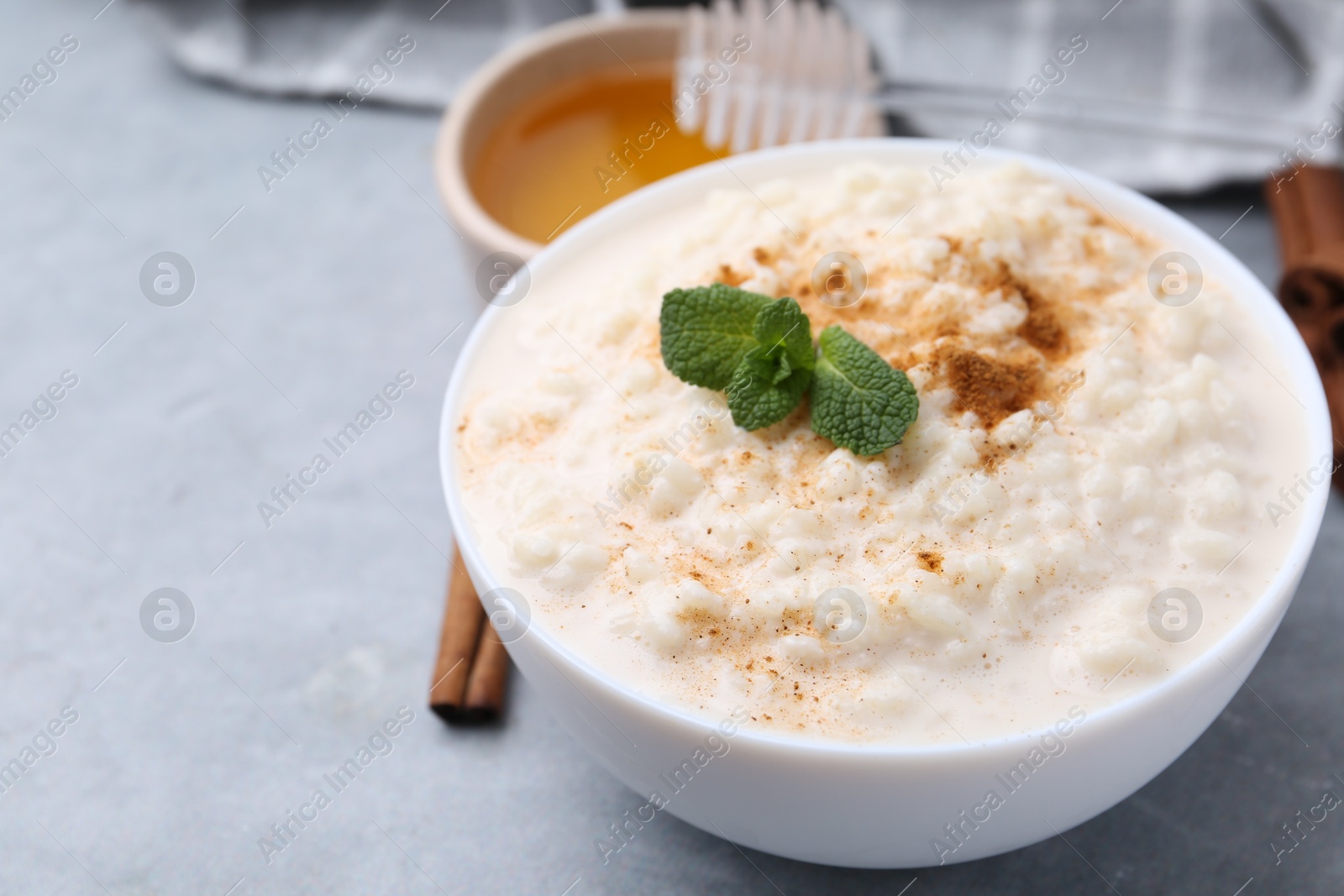 Photo of Tasty rice pudding with cinnamon, mint and honey on light grey table, closeup. Space for text