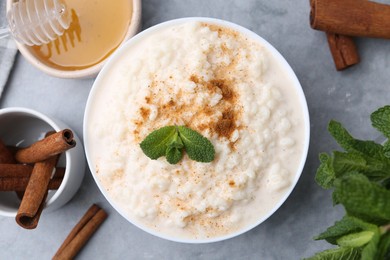 Photo of Tasty rice pudding with cinnamon, mint and honey on light grey table, flat lay