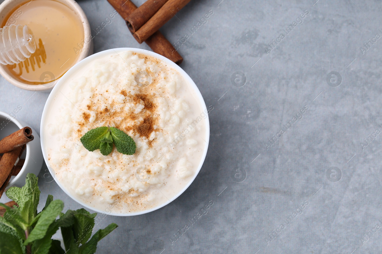 Photo of Tasty rice pudding with cinnamon, mint and honey on light grey table, flat lay. Space for text