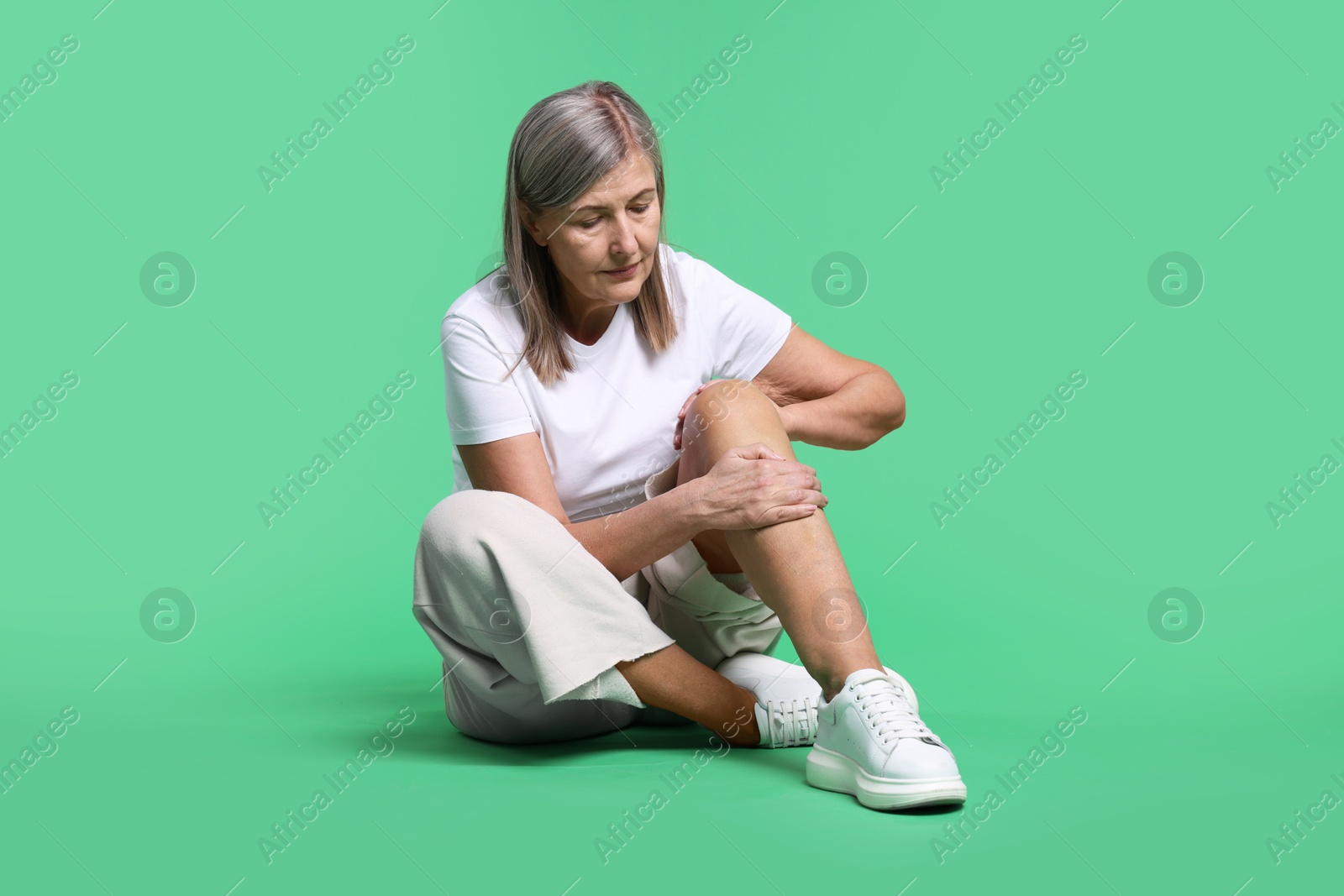 Photo of Senior woman suffering from knee pain on green background