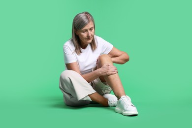 Photo of Senior woman suffering from knee pain on green background