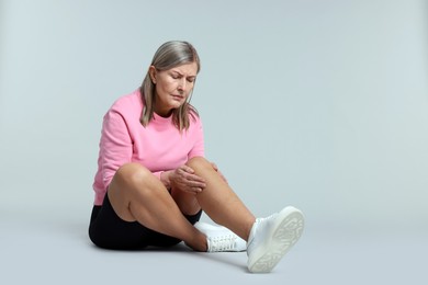 Photo of Senior woman suffering from knee pain on light grey background. Space for text