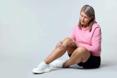 Photo of Senior woman suffering from knee pain on light grey background. Space for text