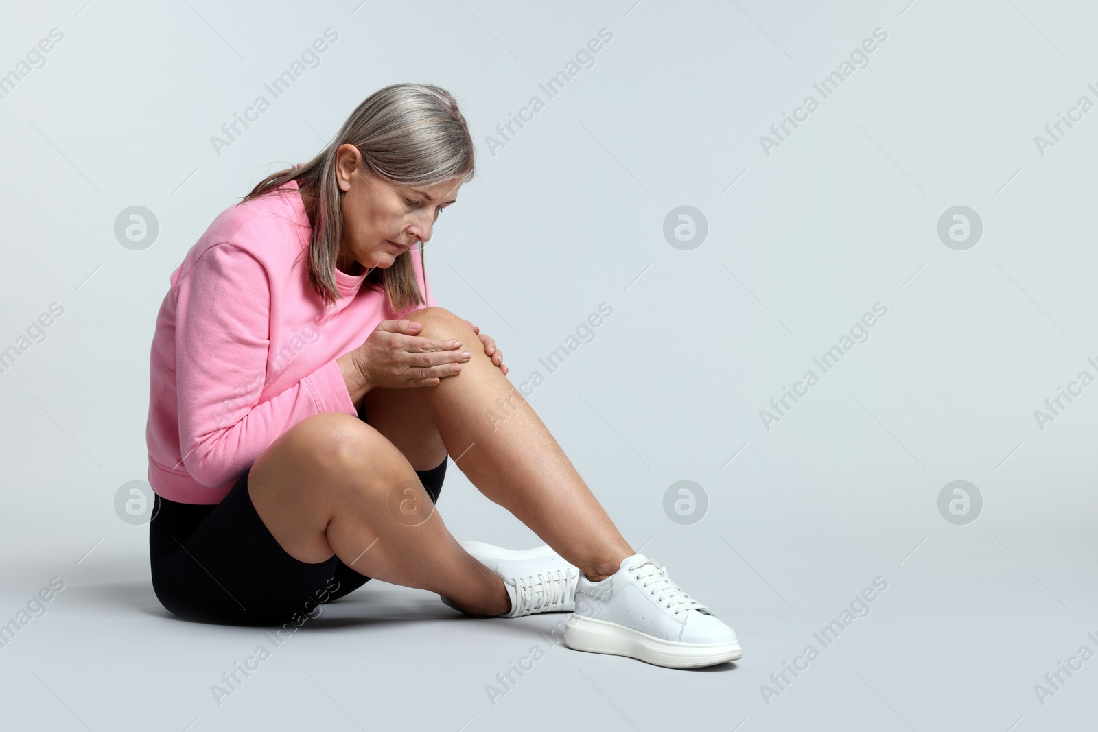 Photo of Senior woman suffering from knee pain on light grey background. Space for text