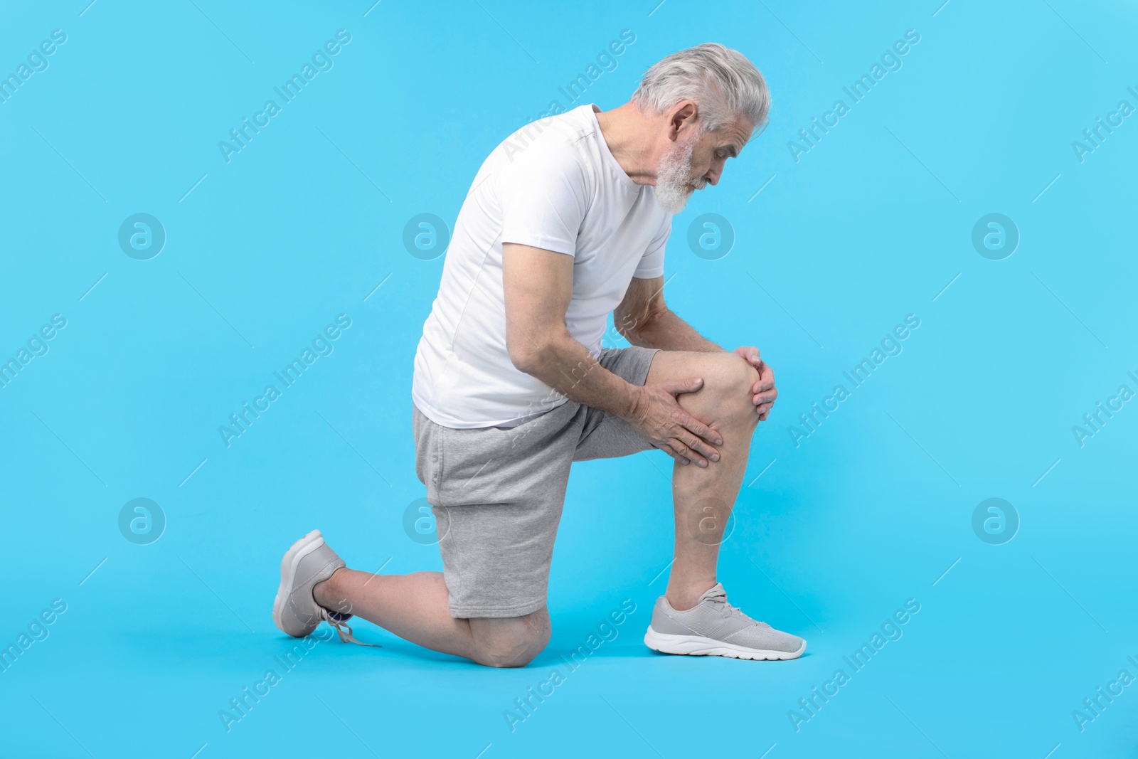 Photo of Senior man suffering from pain in his knee on light blue background