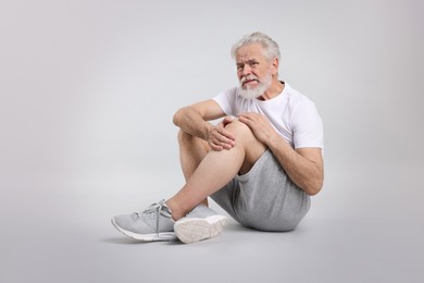 Photo of Senior man suffering from pain in his knee on light background