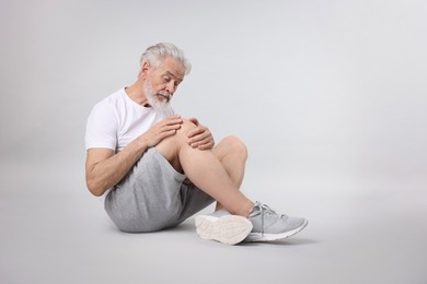 Photo of Senior man suffering from pain in his knee on light background. Space for text