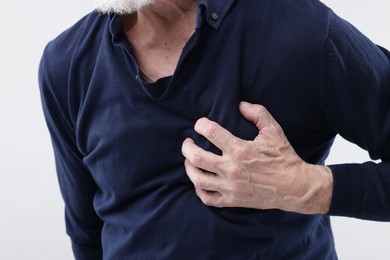 Photo of Heart attack. Senior man suffering from pain in chest on light background, closeup