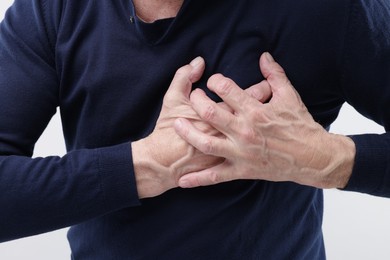 Photo of Heart attack. Senior man suffering from pain in chest on light background, closeup