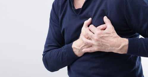 Heart attack. Senior man suffering from pain in chest on light background, closeup. Space for text