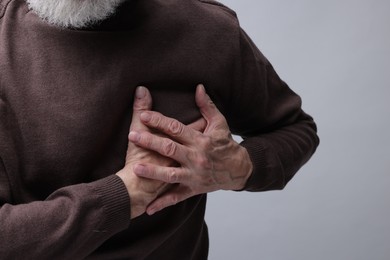 Photo of Heart attack. Senior man suffering from pain in chest on grey background, closeup