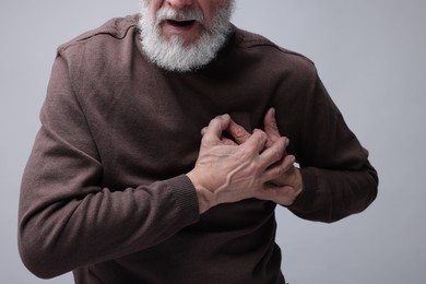 Heart attack. Senior man suffering from pain in chest on grey background, closeup