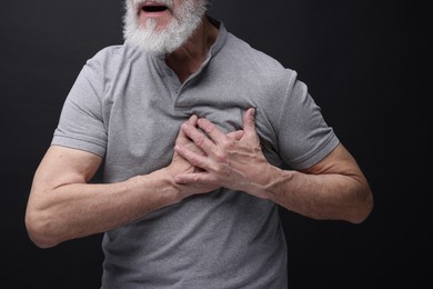 Heart attack. Senior man suffering from pain in chest on black background, closeup