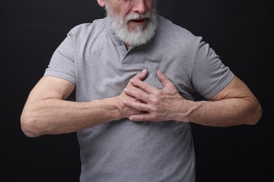 Heart attack. Senior man suffering from pain in chest on black background, closeup