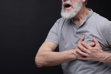 Heart attack. Senior man suffering from pain in chest on black background, closeup. Space for text