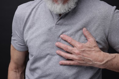 Photo of Heart attack. Senior man suffering from pain in chest on black background, closeup