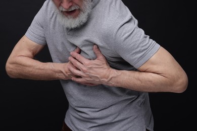 Heart attack. Senior man suffering from pain in chest on black background, closeup