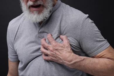 Heart attack. Senior man suffering from pain in chest on black background, closeup