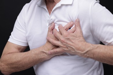 Photo of Heart attack. Senior man suffering from pain in chest on black background, closeup