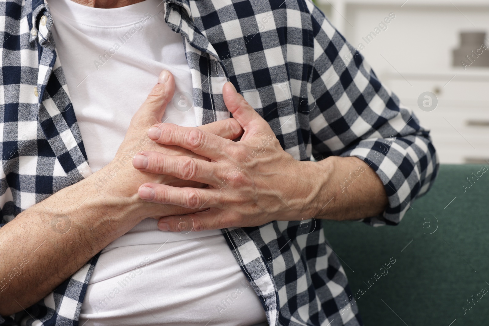 Photo of Heart attack. Senior man suffering from pain in chest on sofa at home, closeup