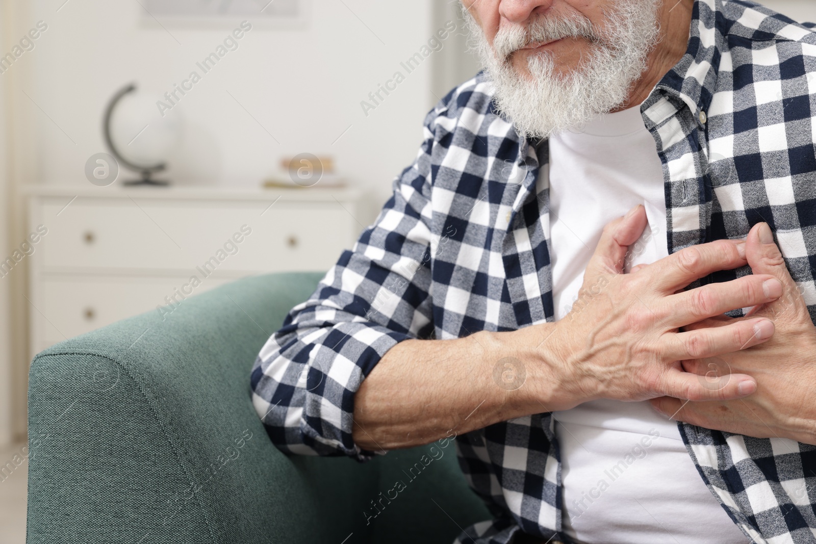 Photo of Heart attack. Senior man suffering from pain in chest on sofa at home, closeup