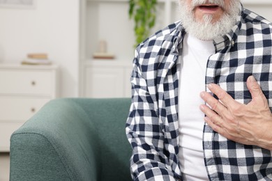 Photo of Heart attack. Senior man suffering from pain in chest on sofa at home, closeup