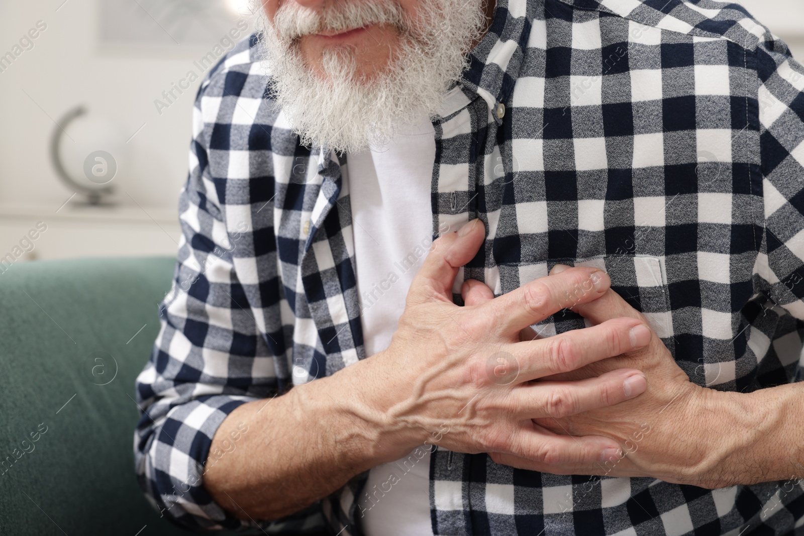 Photo of Heart attack. Senior man suffering from pain in chest on sofa at home, closeup