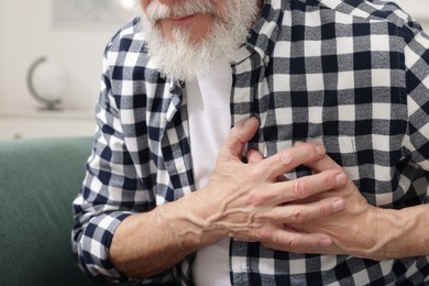 Heart attack. Senior man suffering from pain in chest on sofa at home, closeup