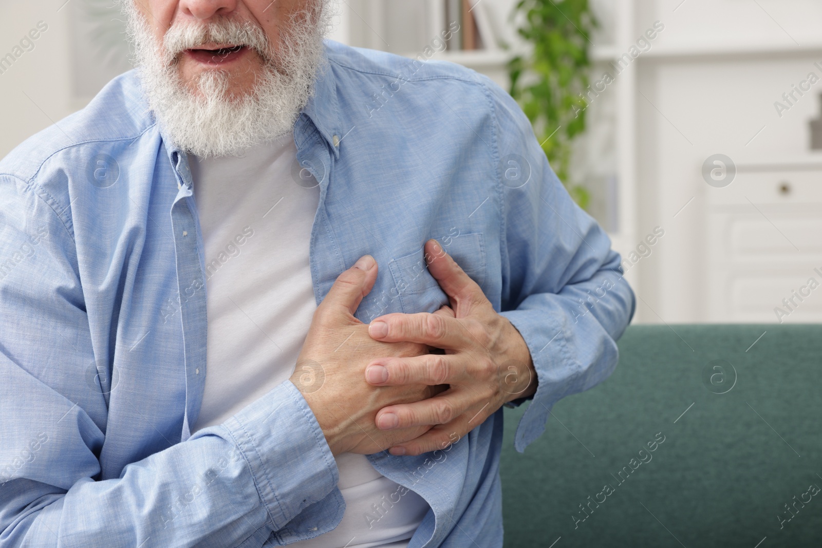 Photo of Heart attack. Senior man suffering from pain in chest on sofa at home, closeup