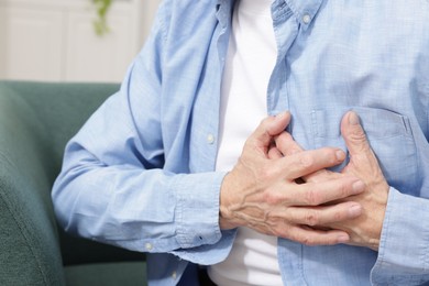 Photo of Heart attack. Senior man suffering from pain in chest on sofa at home, closeup