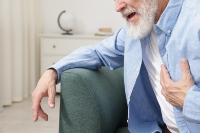 Photo of Heart attack. Senior man suffering from pain in chest on sofa at home, closeup