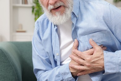 Photo of Heart attack. Senior man suffering from pain in chest on sofa at home, closeup