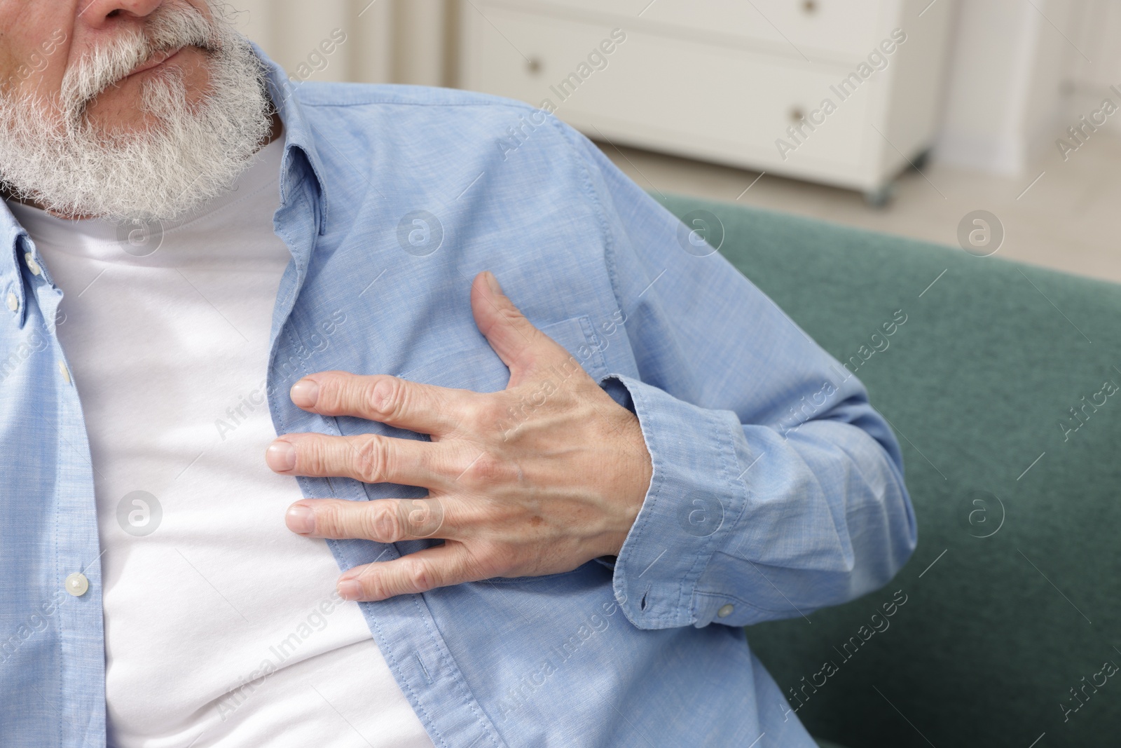 Photo of Heart attack. Senior man suffering from pain in chest on sofa at home, closeup