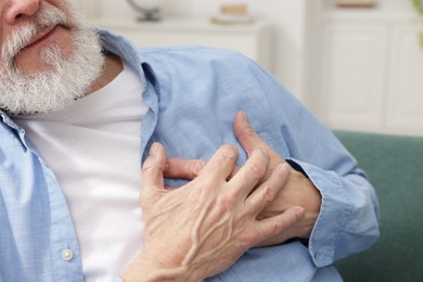 Photo of Heart attack. Senior man suffering from pain in chest on sofa at home, closeup