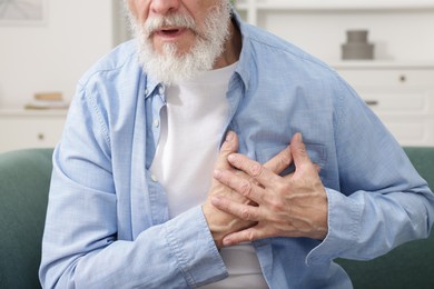 Heart attack. Senior man suffering from pain in chest on sofa at home, closeup