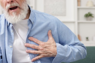 Photo of Heart attack. Senior man suffering from pain in chest on sofa at home, closeup