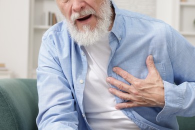 Photo of Heart attack. Senior man suffering from pain in chest on sofa at home, closeup